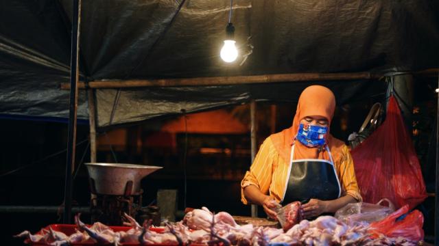 Indonesian woman packs chicken meat for sale at a night market. Photo credit: iStock/gamalis.